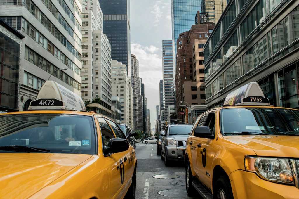 Image of street in New York City with 2 taxi cabs waiting for a light to change. Background shows buildings, including a McDonald's sign visible in the distance.