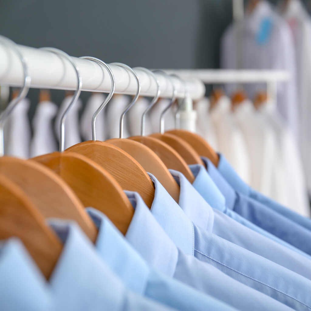 Neatly pressed blue dress shirts hanging on wooden hangers in a clean, organized row.