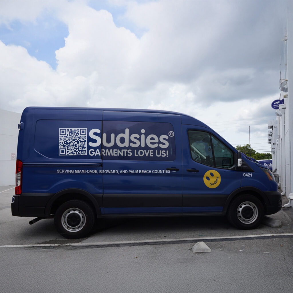 Blue Sudsies delivery van parked outside the facility with branding and service area details