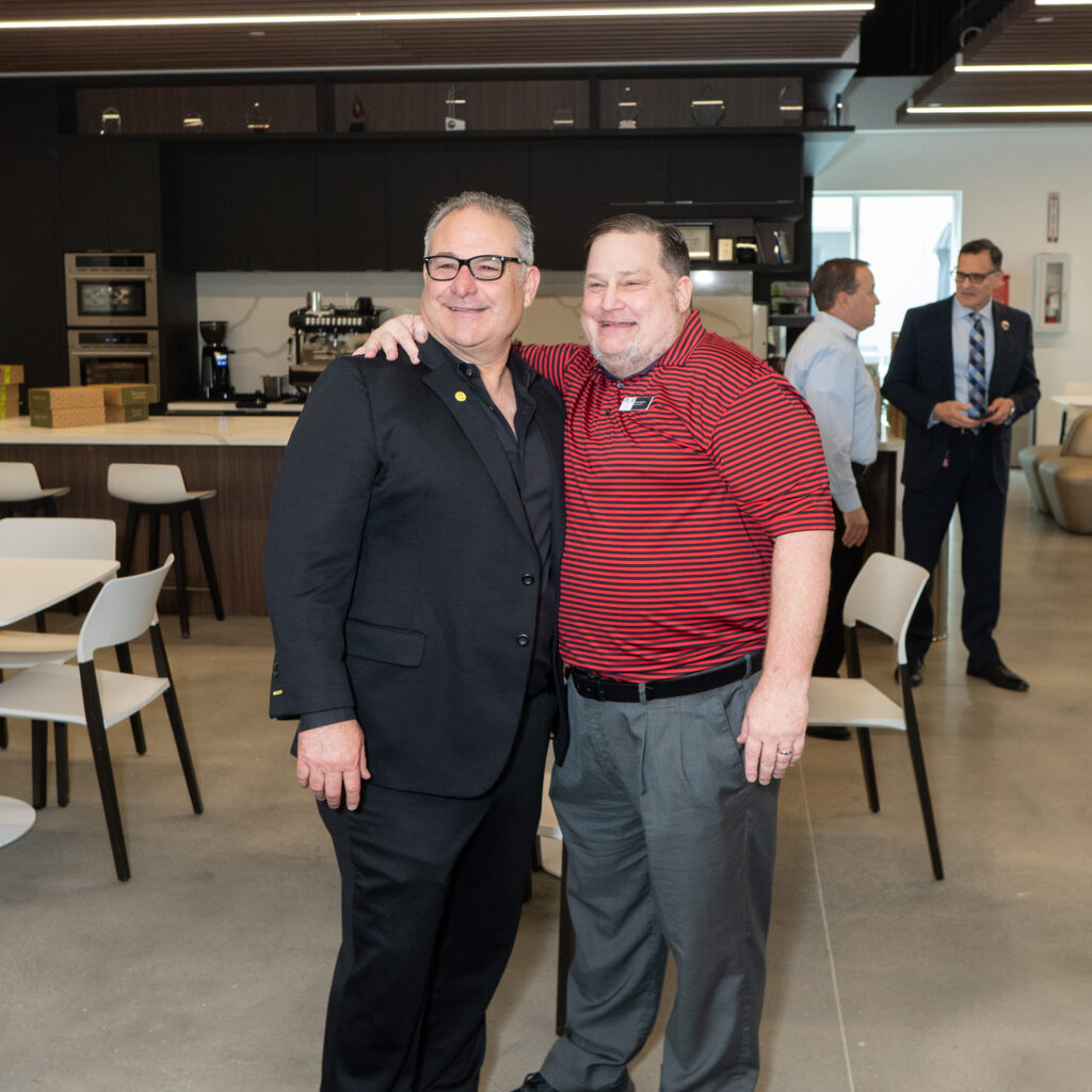 Two colleagues smiling and posing together in an office café setting.