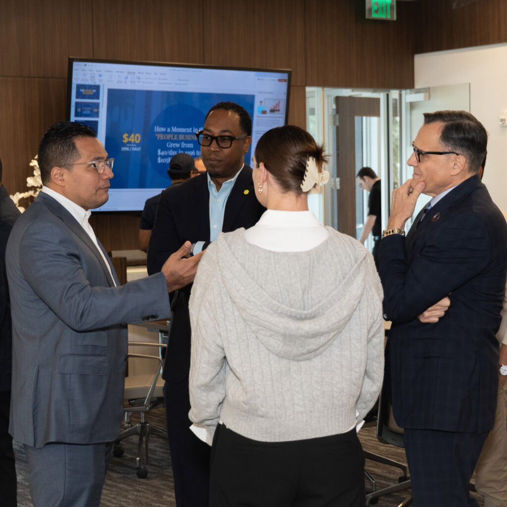 Group of professionals in conversation during an office meeting, standing together near a presentation screen.