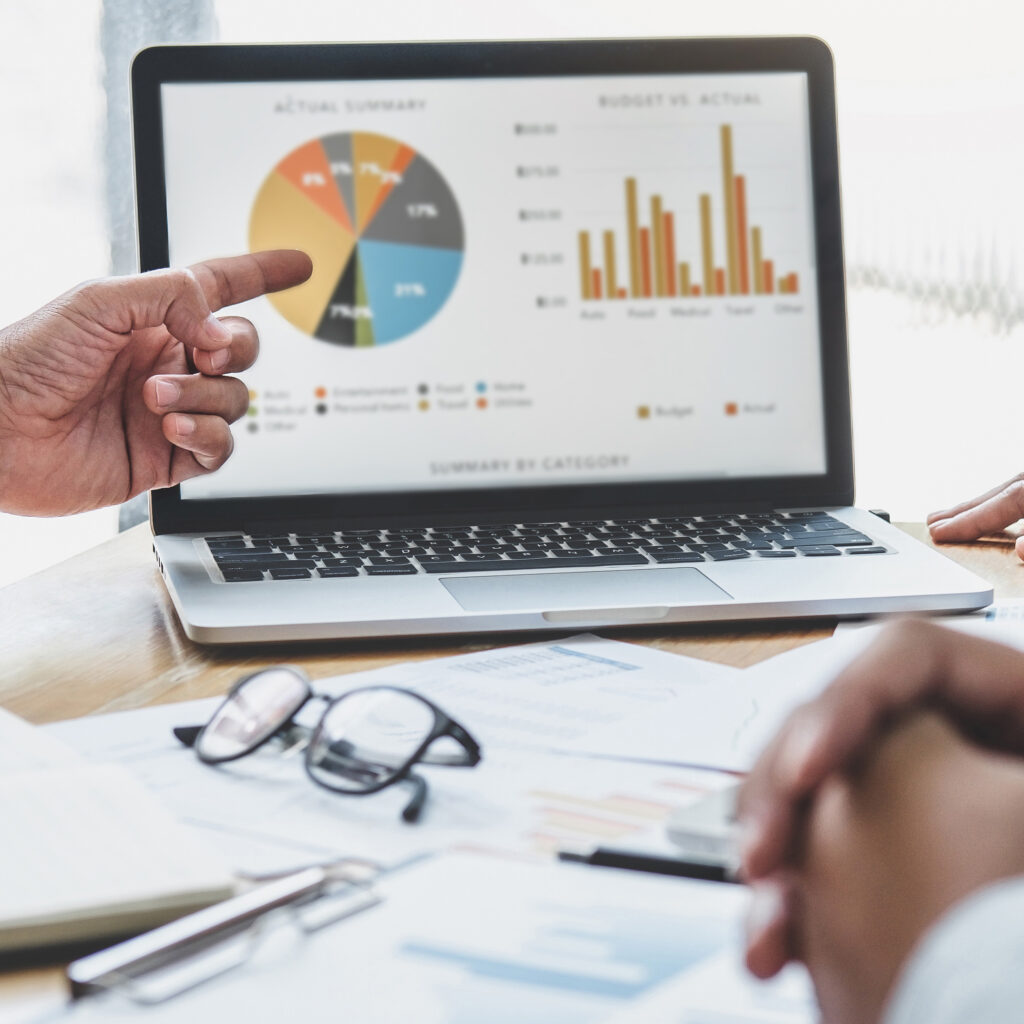 Hands pointing at a laptop showing charts and budget vs actual data
